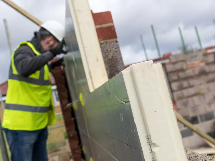 Worker in safety gear building a brick wall on a construction site.