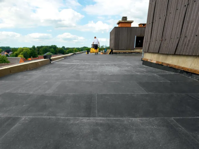 Flat rooftop with black Eurothane Bi-4 insulation, wooden wall, cloudy sky, and distant figure.
