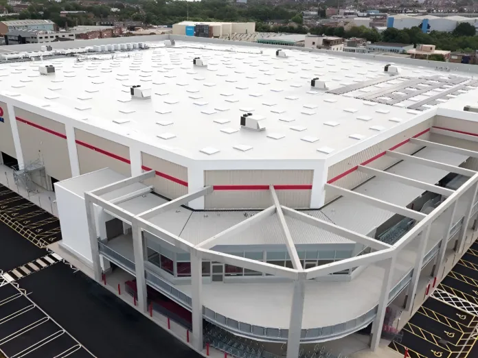 Warehouse exterior with large white roof and parking lot.