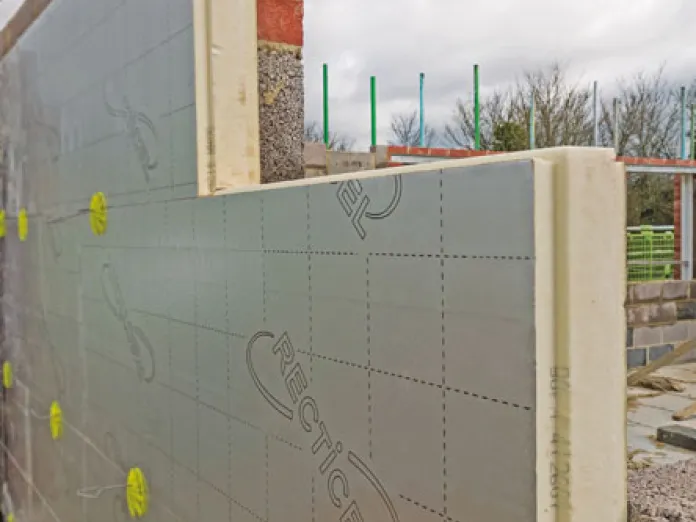 Building wall with insulation panels and brick foundation under a cloudy sky.