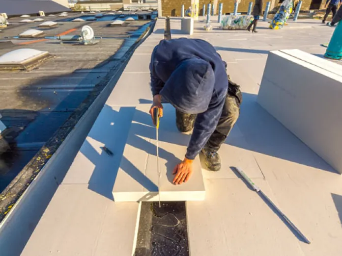 Worker installing insulation on a flat rooftop under blue sky.