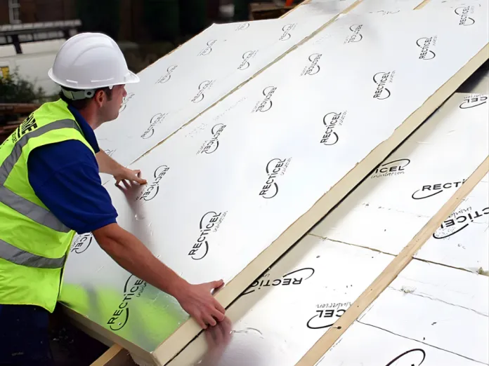 Worker in hard hat installing insulation panels on a roof.