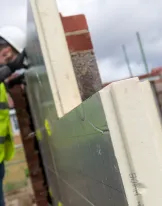 Worker in safety gear building a brick wall on a construction site.