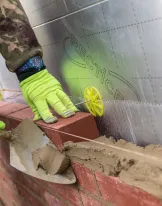 Bricklayer with green gloves applying mortar to a wall.