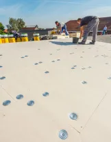 Workers on a flat rooftop installing waterproofing membrane.