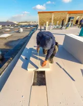 Worker installing insulation on a flat rooftop under blue sky.