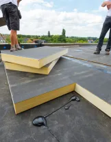 Workers installing insulation panels on a flat rooftop under a blue sky.