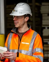 Worker in an orange safety jacket and helmet holding a brick.