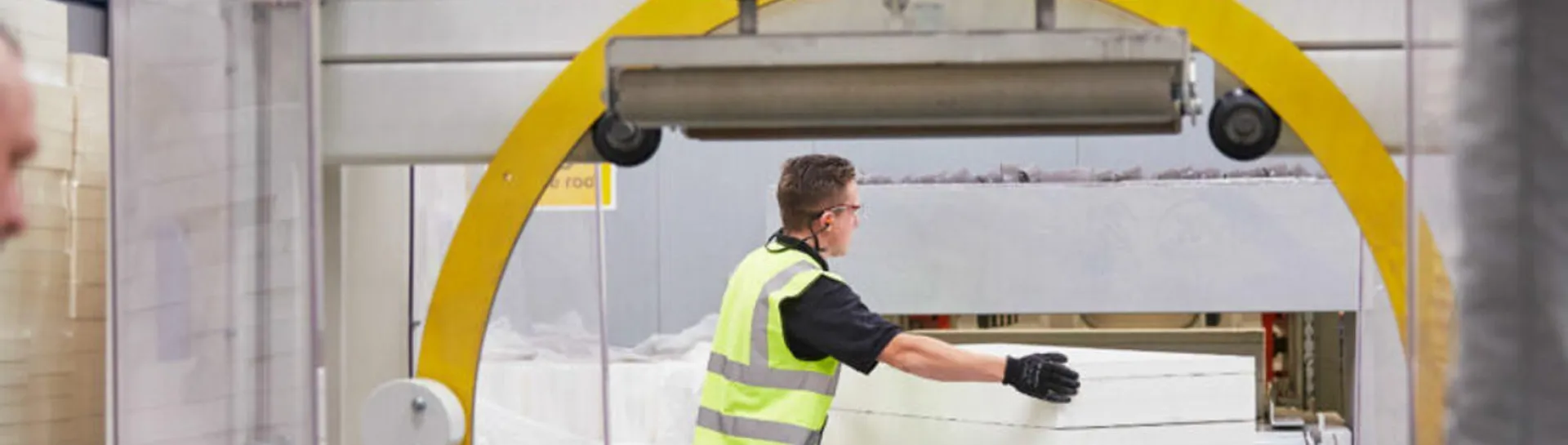 Worker handling materials in a factory, wearing safety vest and gloves.