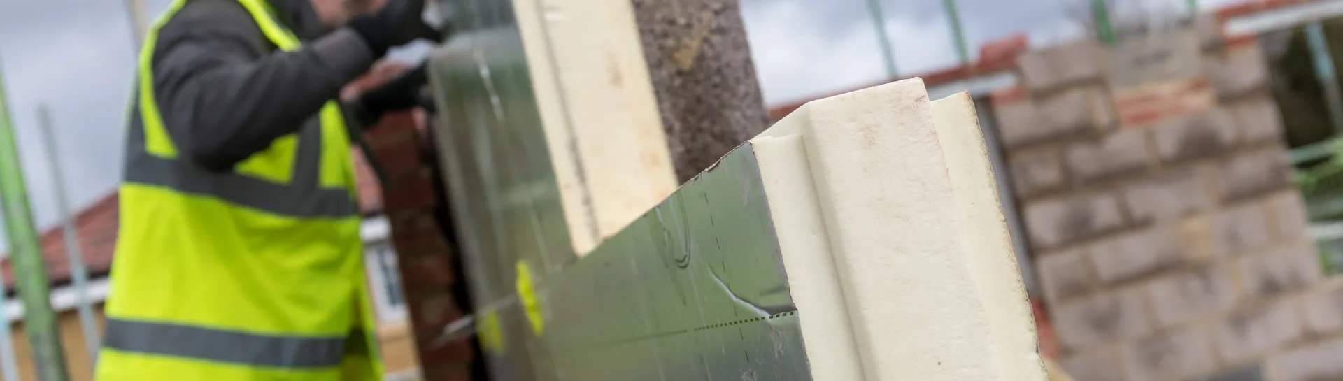 Worker in safety gear building a brick wall on a construction site.