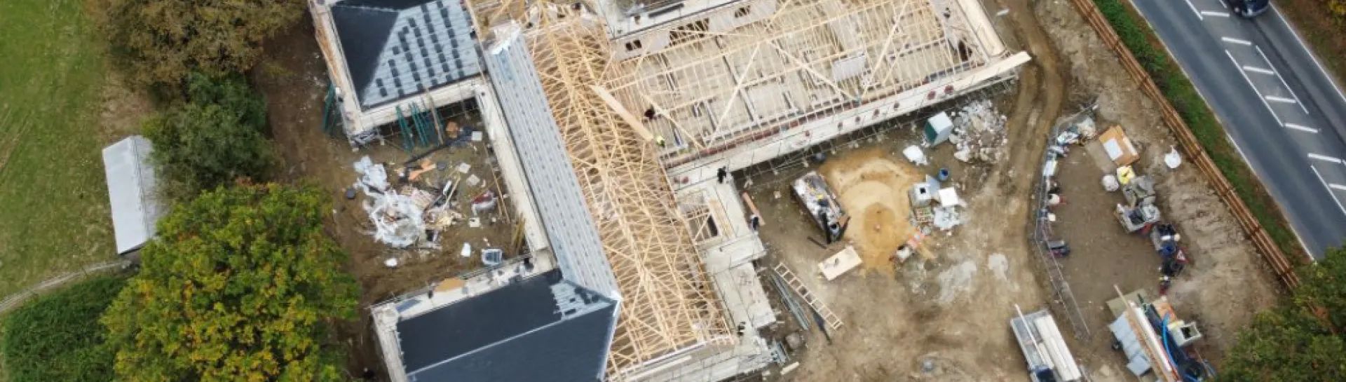 Under-construction building site with vehicles, surrounded by trees and a road.