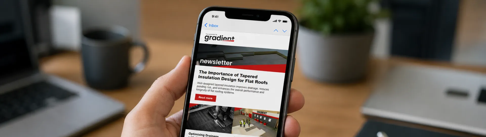 Person holding smartphone displaying a news app, desk items around.