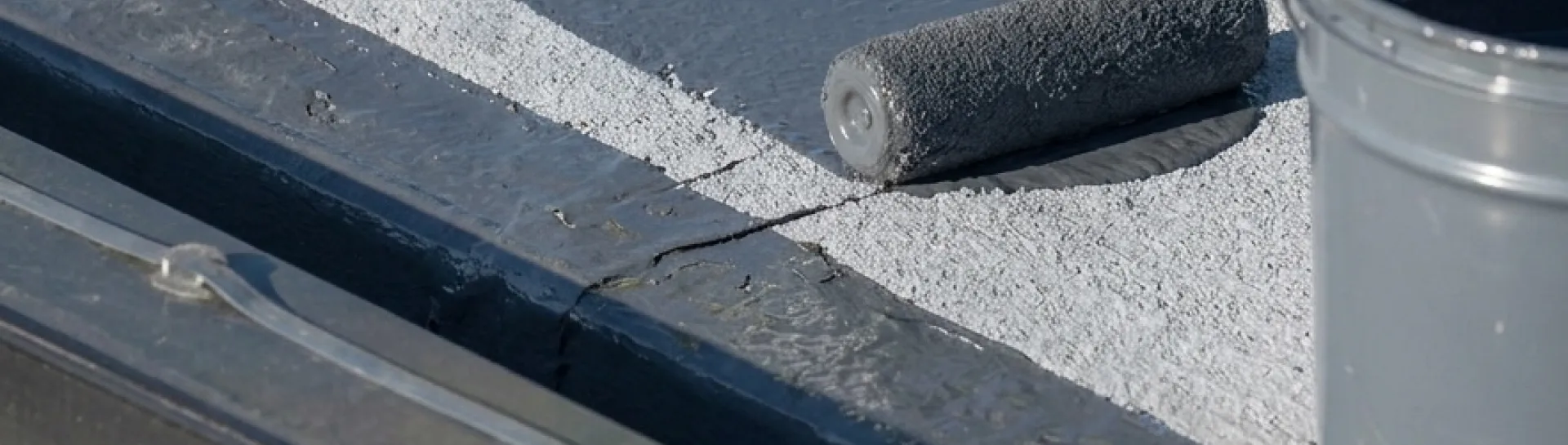Painting a flat roof with a roller and grey paint.