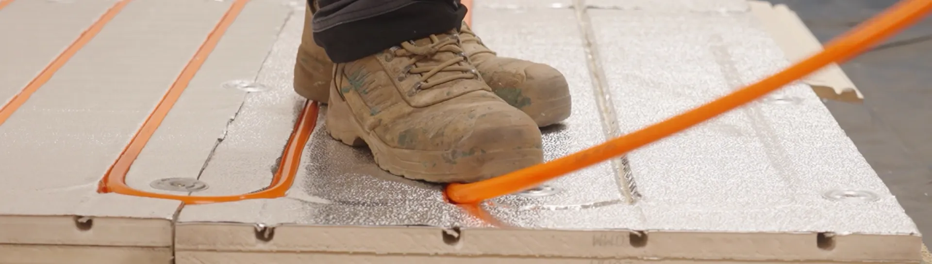 Worker's feet on pipes and panels in construction setting.