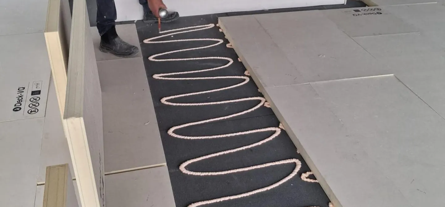 Worker laying heating cables on a floor under construction.