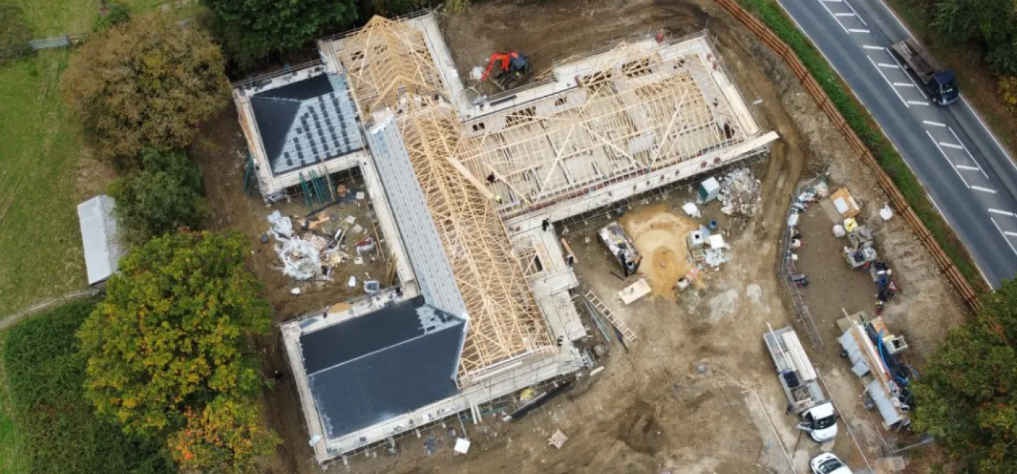 Under-construction building site with vehicles, surrounded by trees and a road.