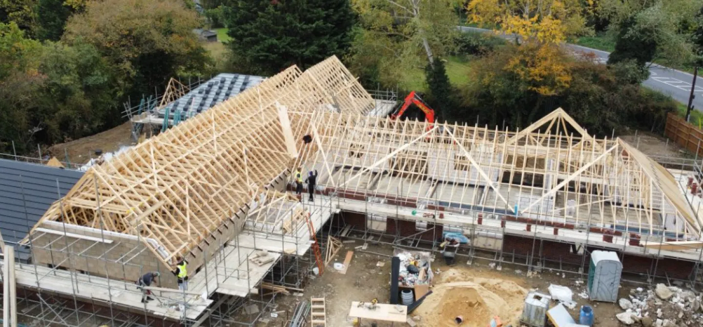 Construction site with wooden roof frameworks surrounded by trees.