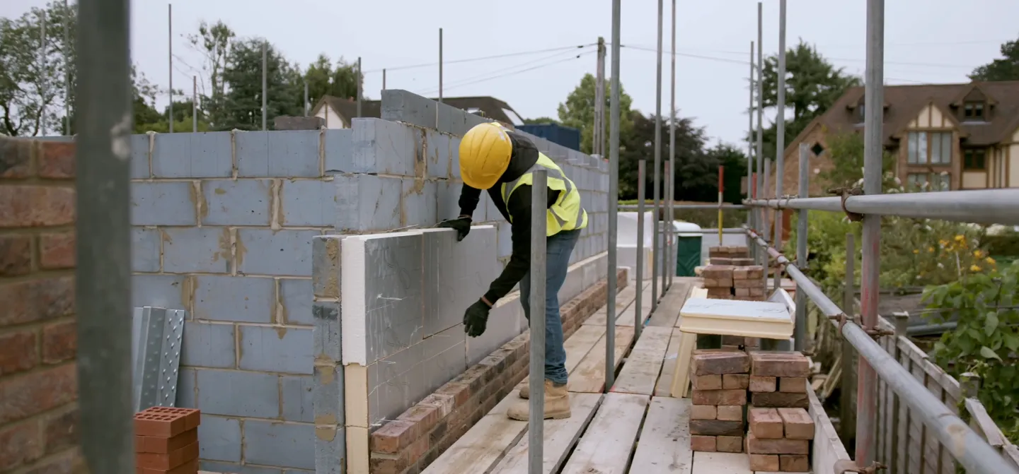 Worker laying bricks on a partially constructed wall, wearing a hard hat.