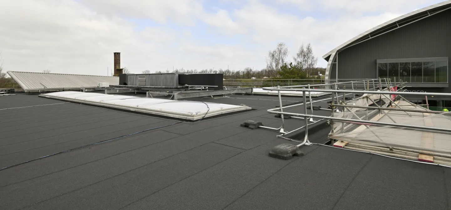 Flat black roof with skylights and safety railings under a cloudy sky.