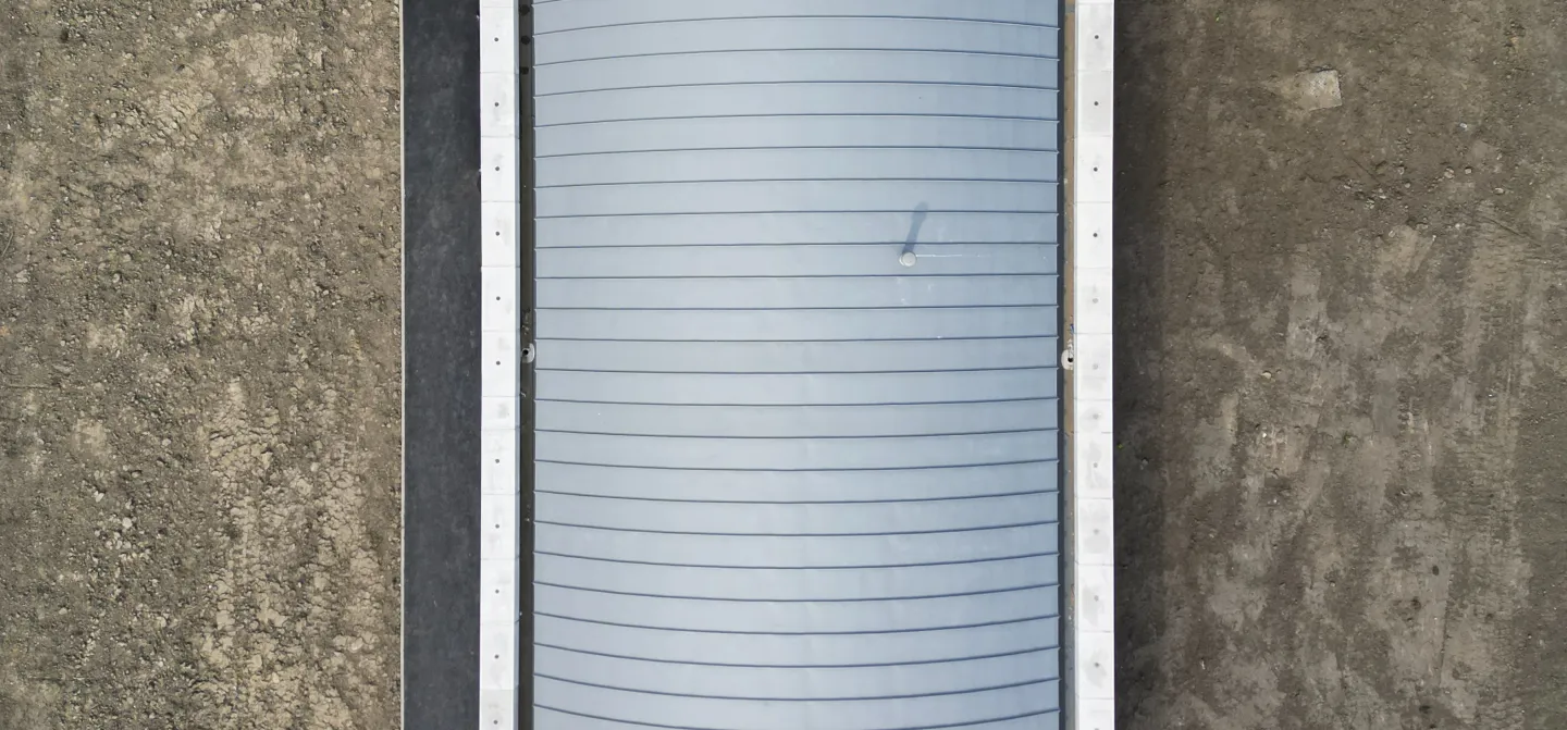 Curved metal structure from above, surrounded by grass and pavement.
