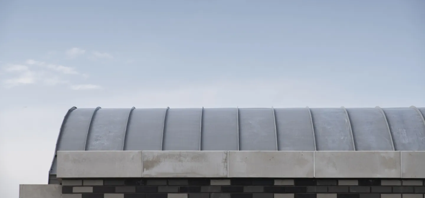 Curved roof of a brick building under a clear blue sky.