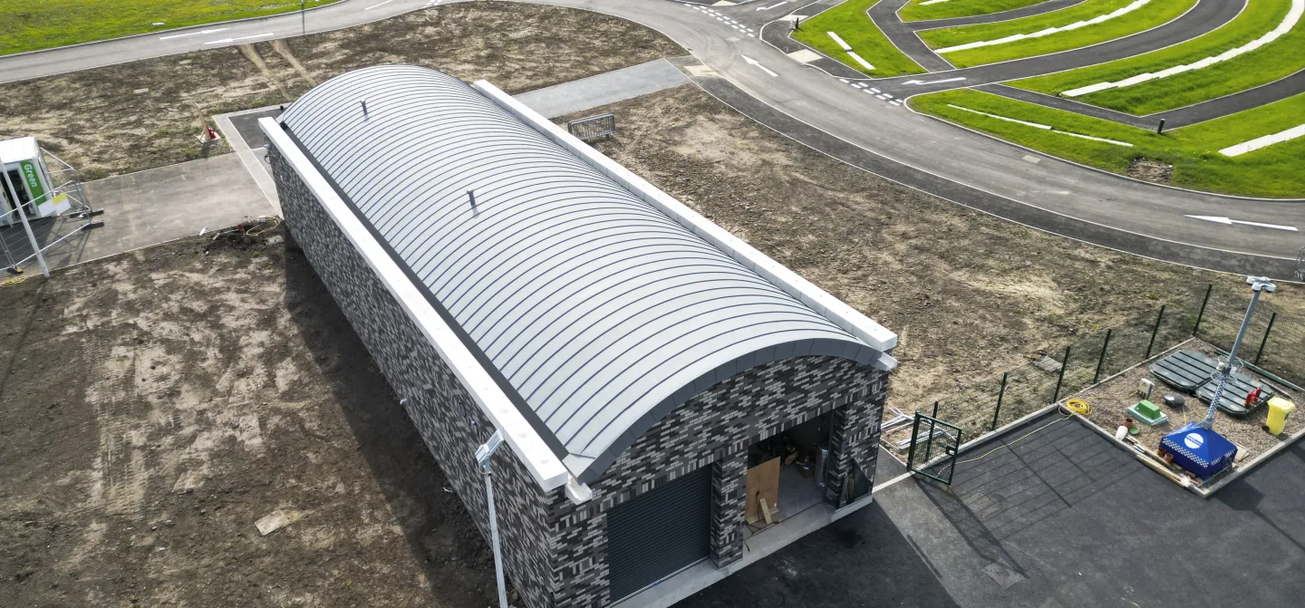 Industrial building with curved roof on landscaped grounds.