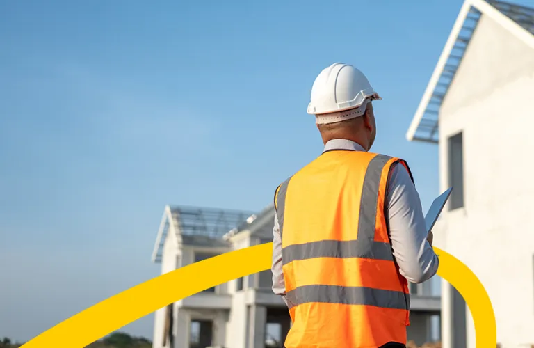 Worker in hard hat and vest inspecting a construction site.