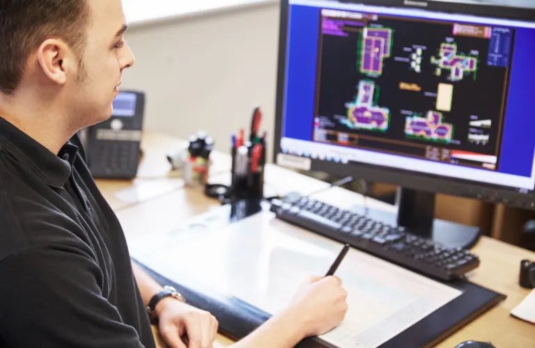 Man working on computer with technical drawings on screen.