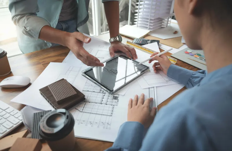 Two people discuss architectural plans at a desk.