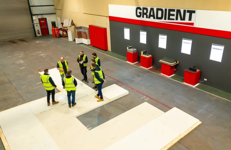Workers in high-vis jackets standing in a warehouse, near signs marked "GRADIENT".