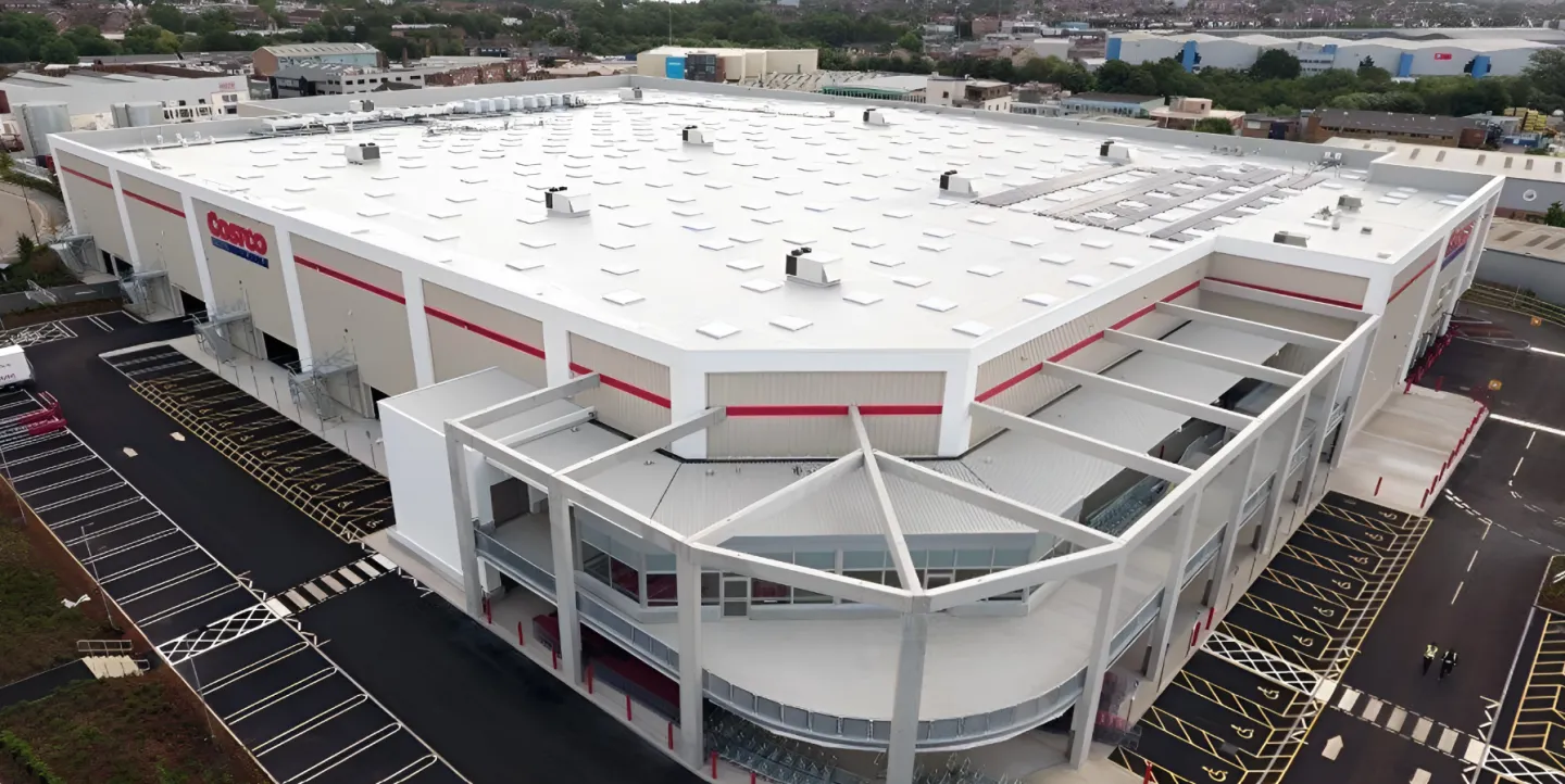Warehouse exterior with large white roof and parking lot.