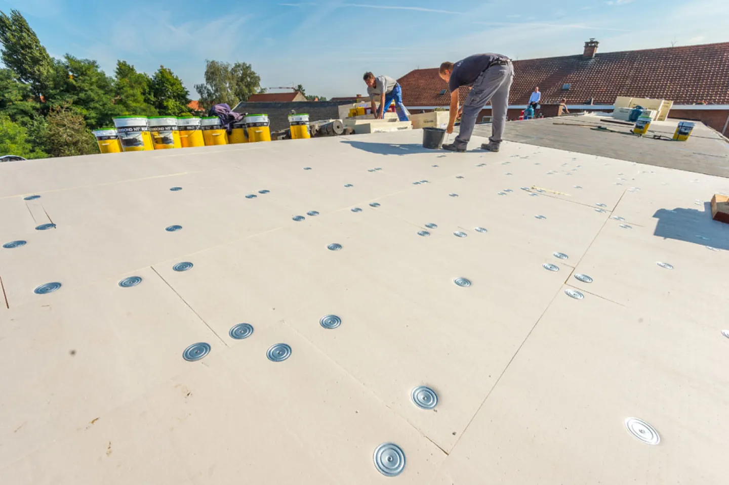 Workers on a flat rooftop installing waterproofing membrane.