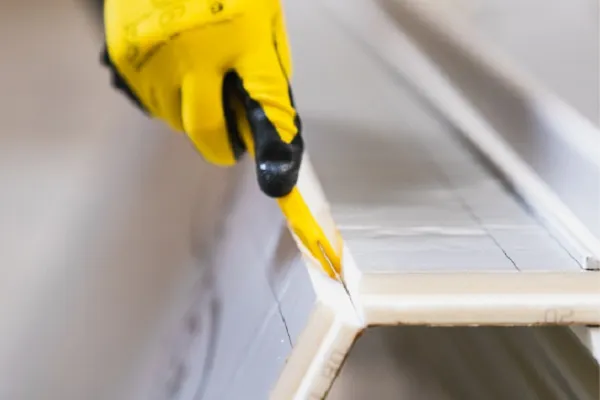 Gloved hand cutting cardboard with a yellow utility knife.