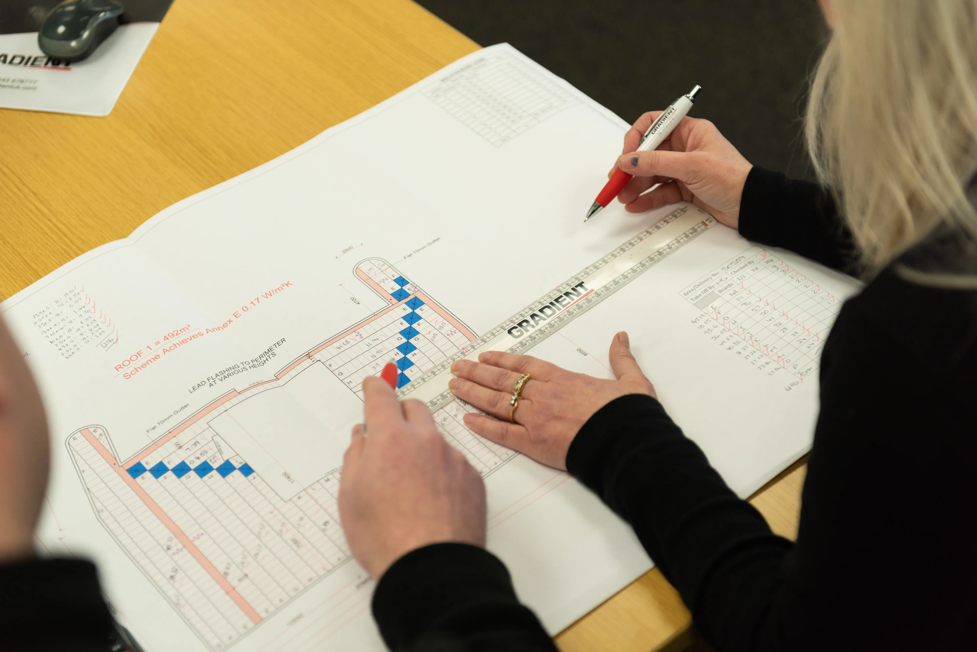 Hands pointing and writing on architectural plans at a table.