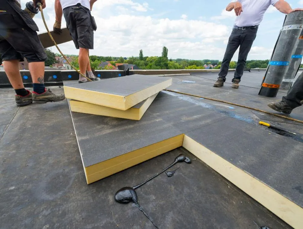 Workers installing insulation panels on a flat roof.