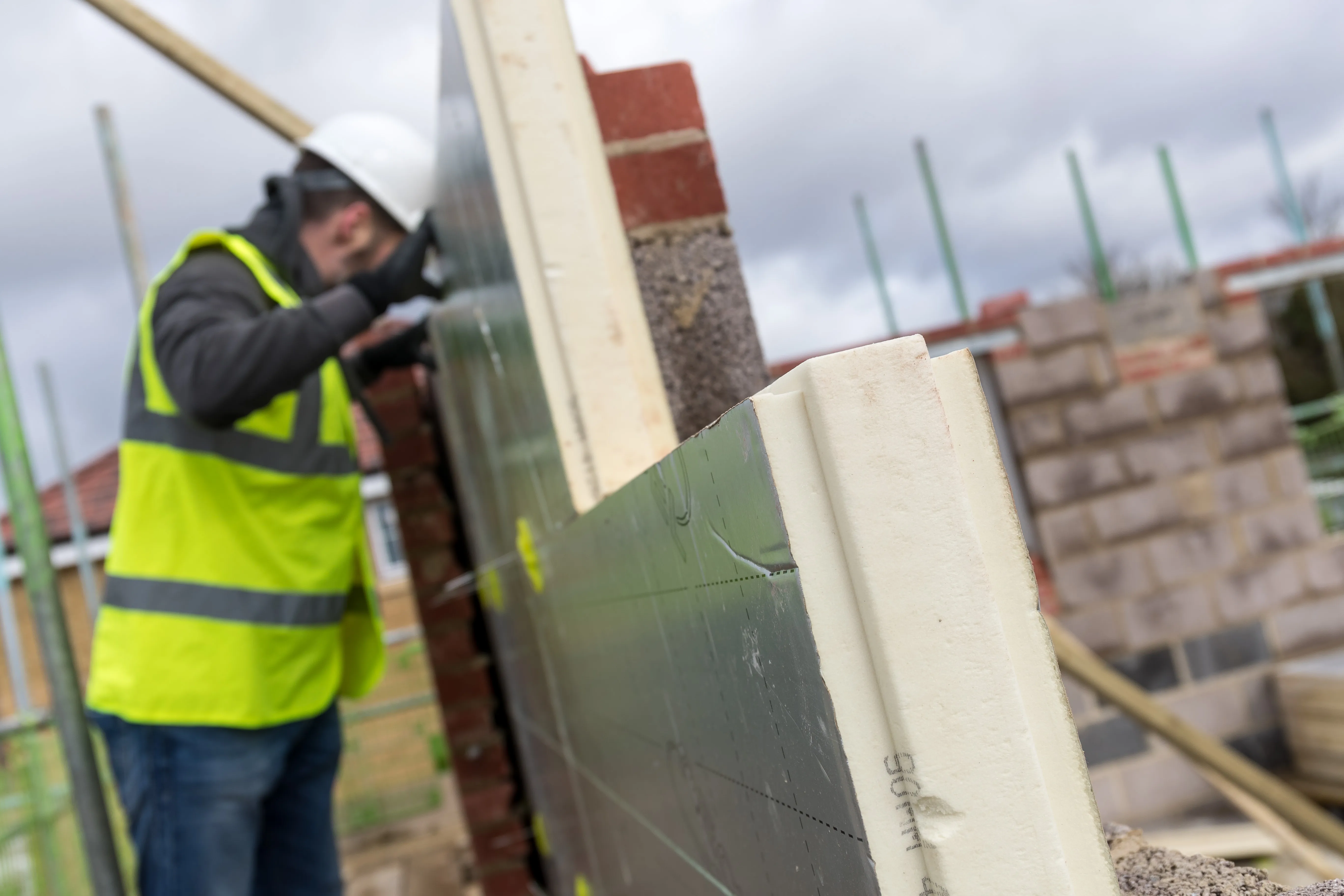 Worker in safety gear building a brick wall on a construction site.