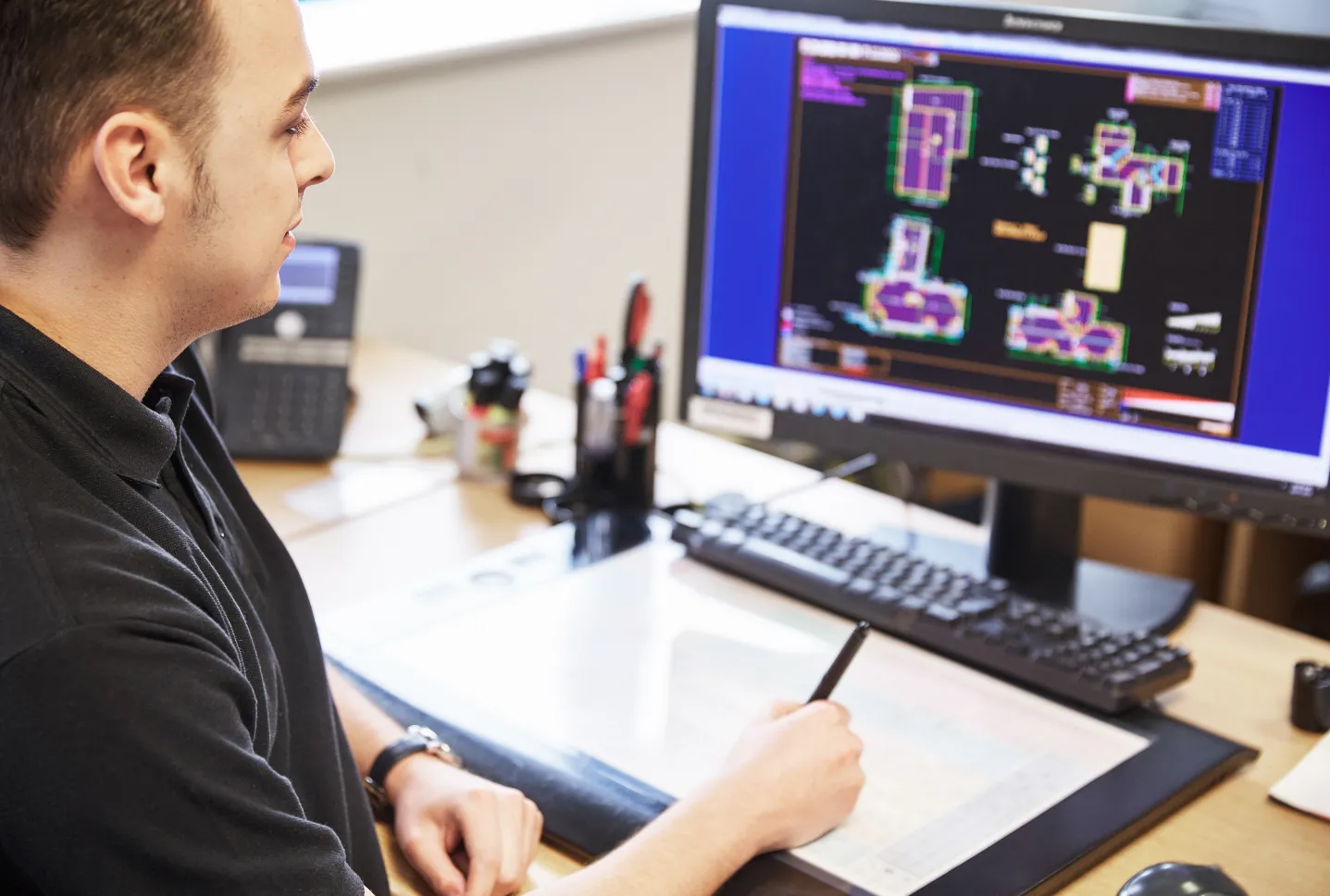 Man working on computer with technical drawings on screen.