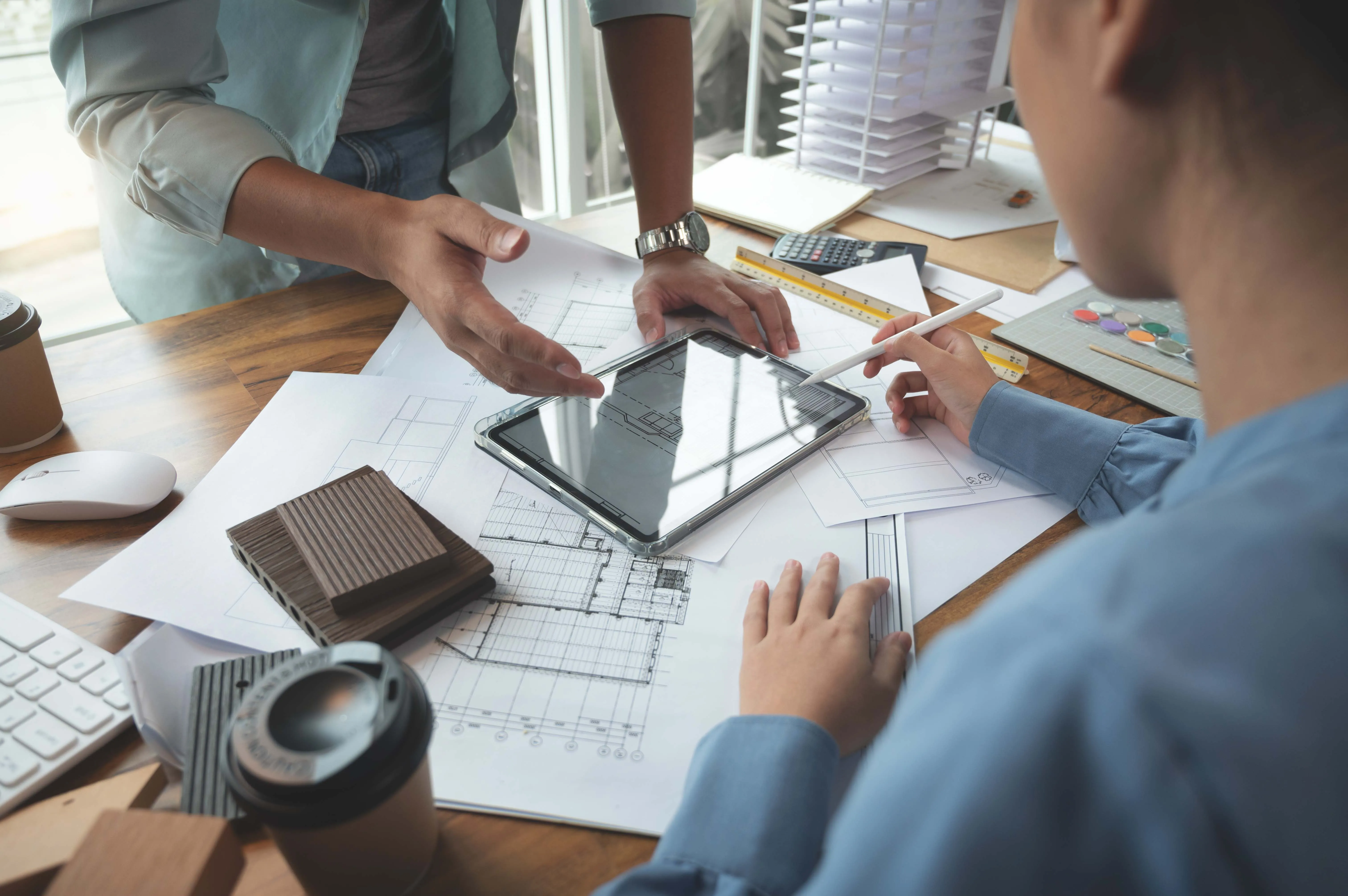 Two people discuss architectural plans at a desk.