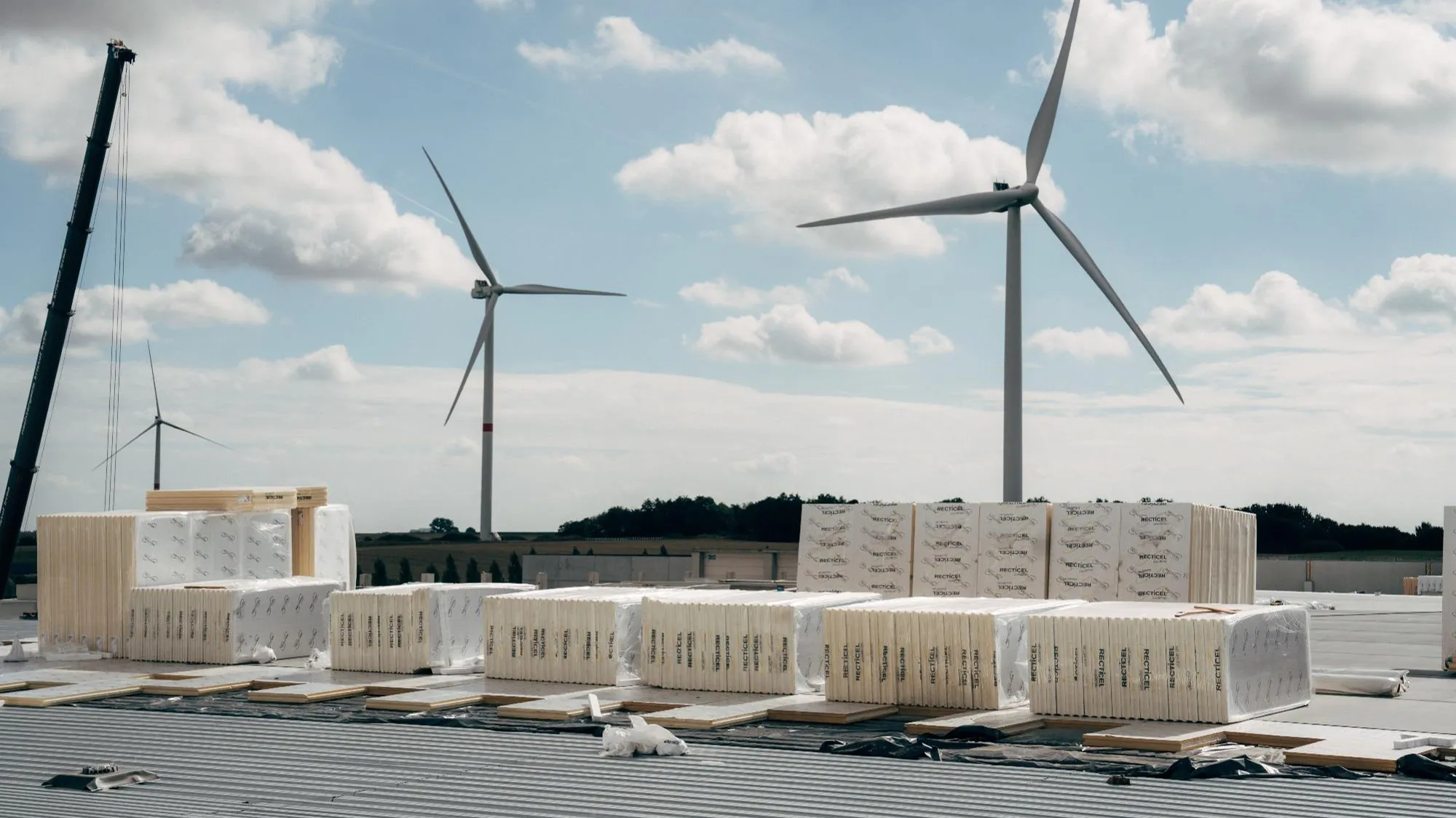 Wind turbines behind construction materials under blue skies.