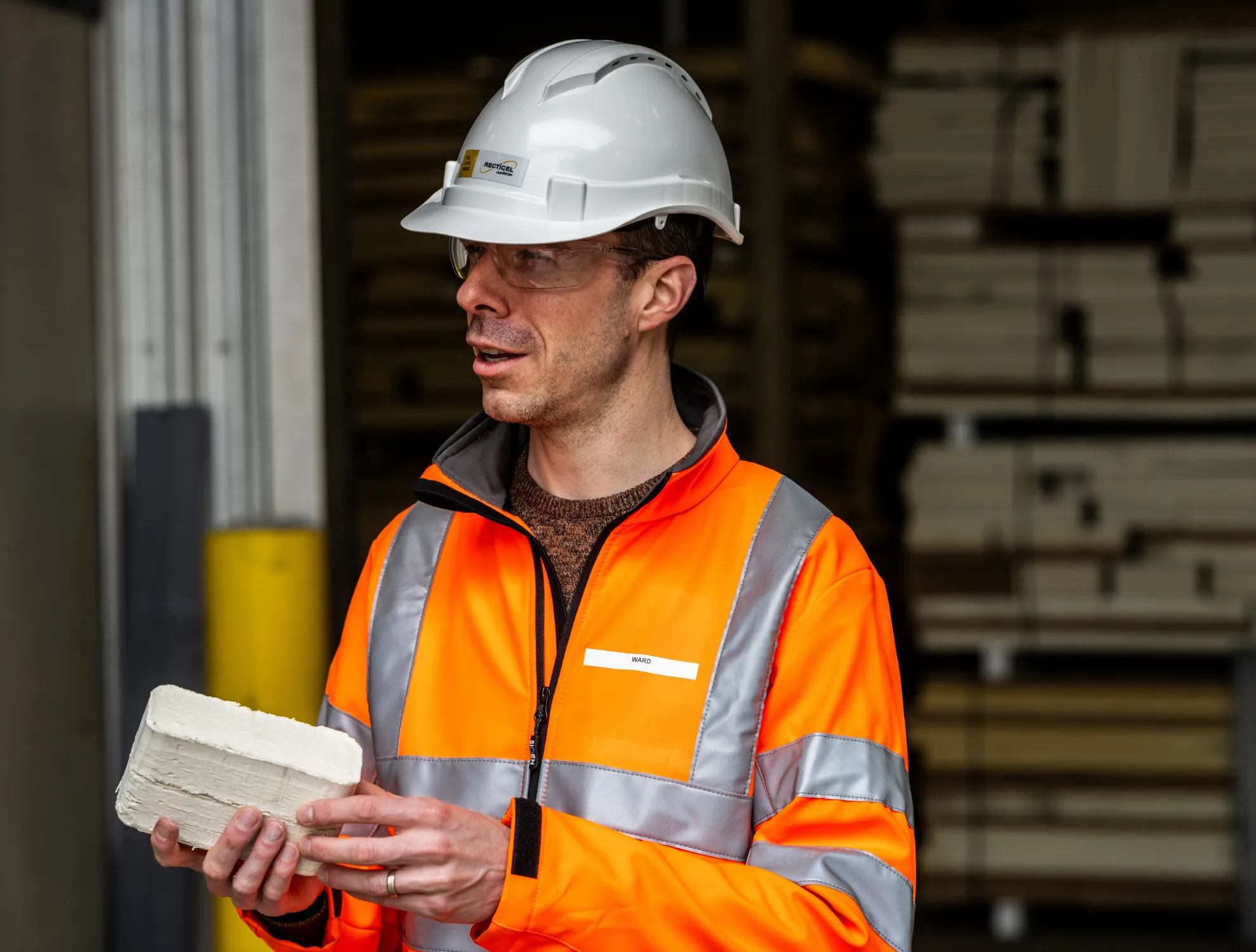Worker in an orange safety jacket and helmet holding a brick.