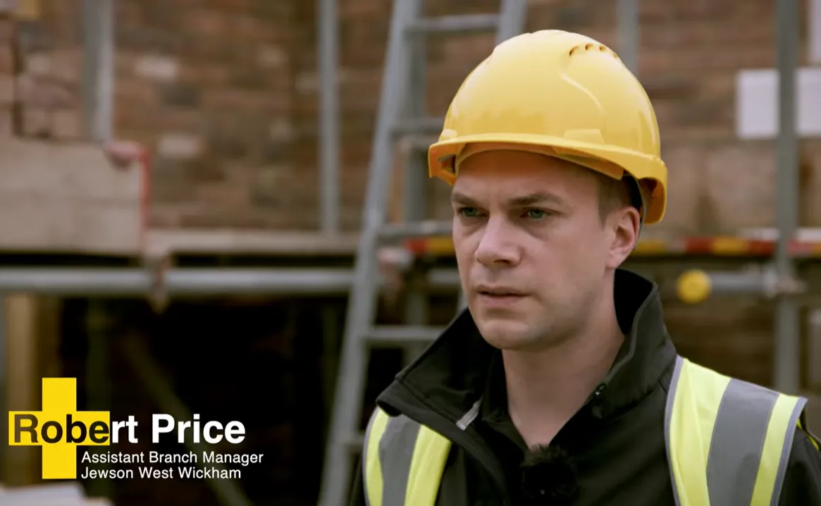 Construction worker in a yellow hard hat and vest at a building site.