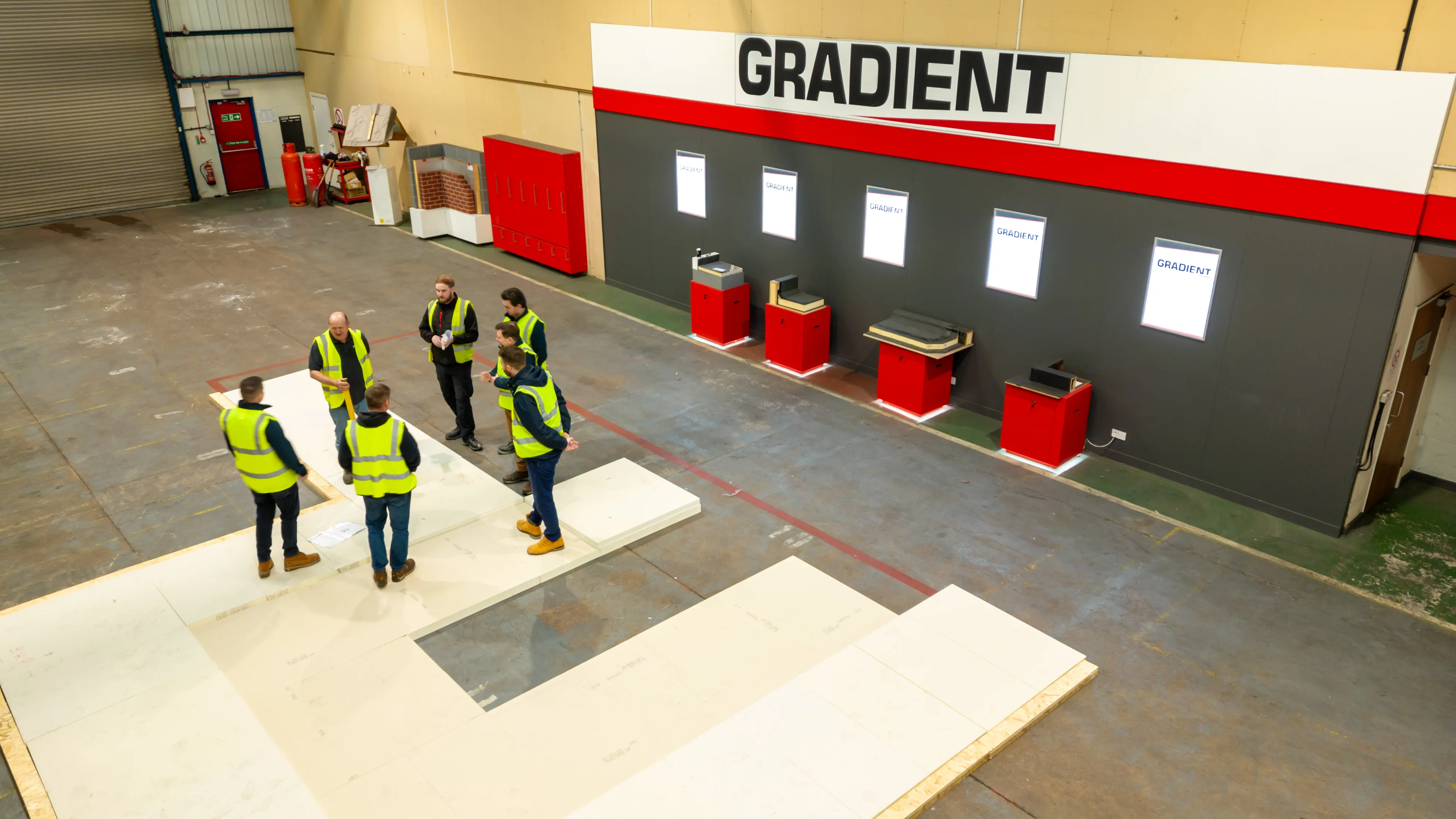 Workers in high-vis jackets standing in a warehouse, near signs marked "GRADIENT".