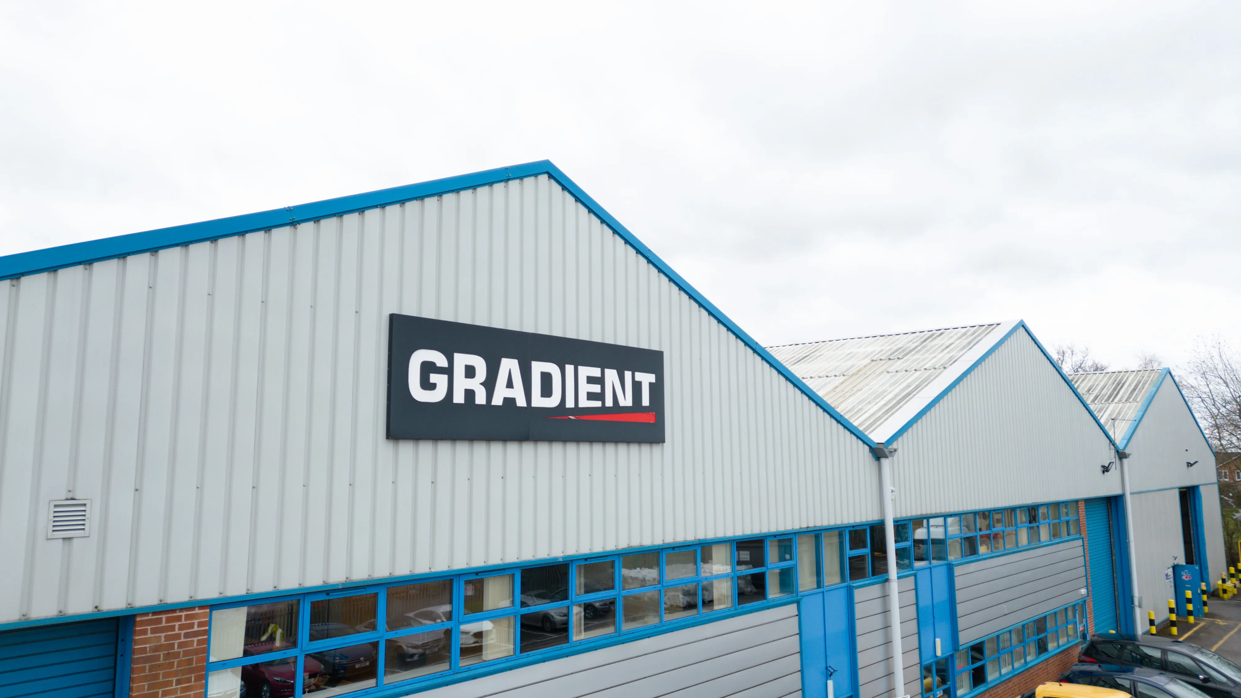 Warehouse with blue trim and "GRADIENT" sign. Cloudy sky above.
