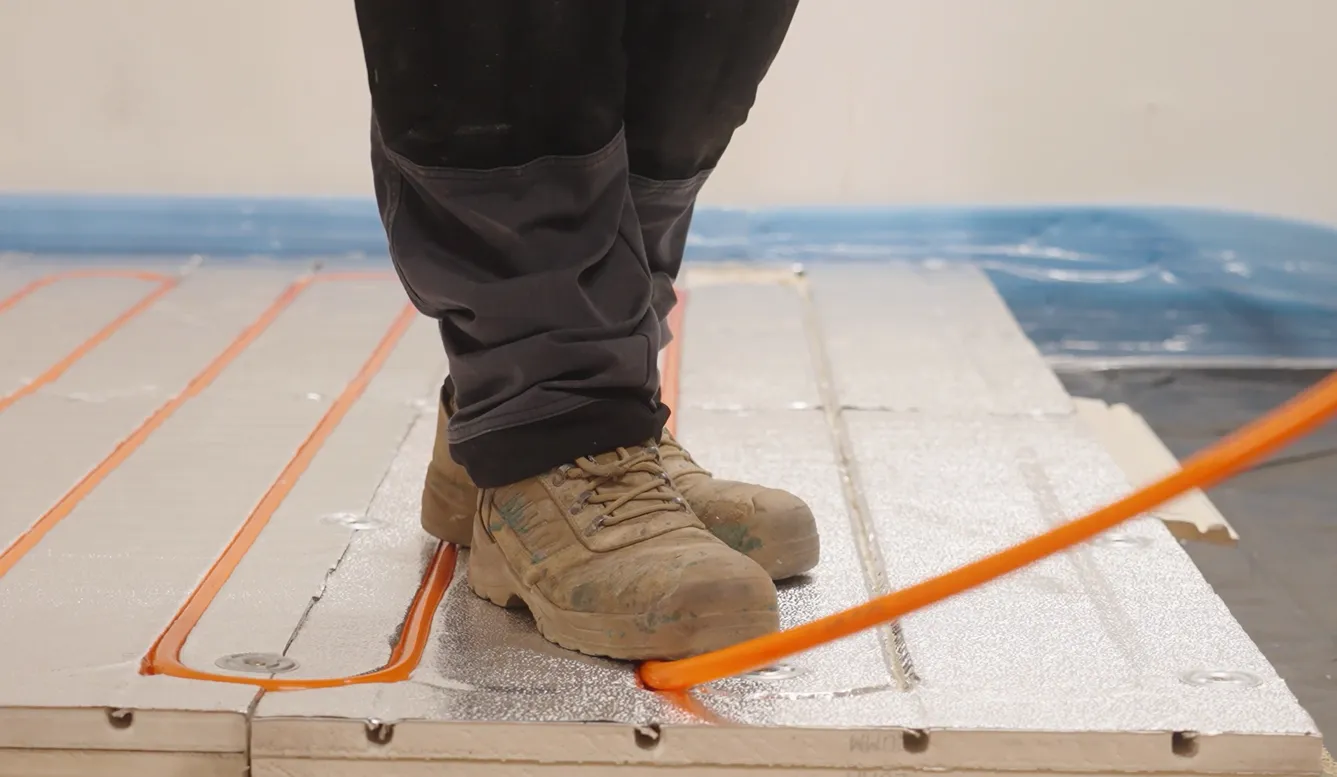 Worker's feet on pipes and panels in construction setting.