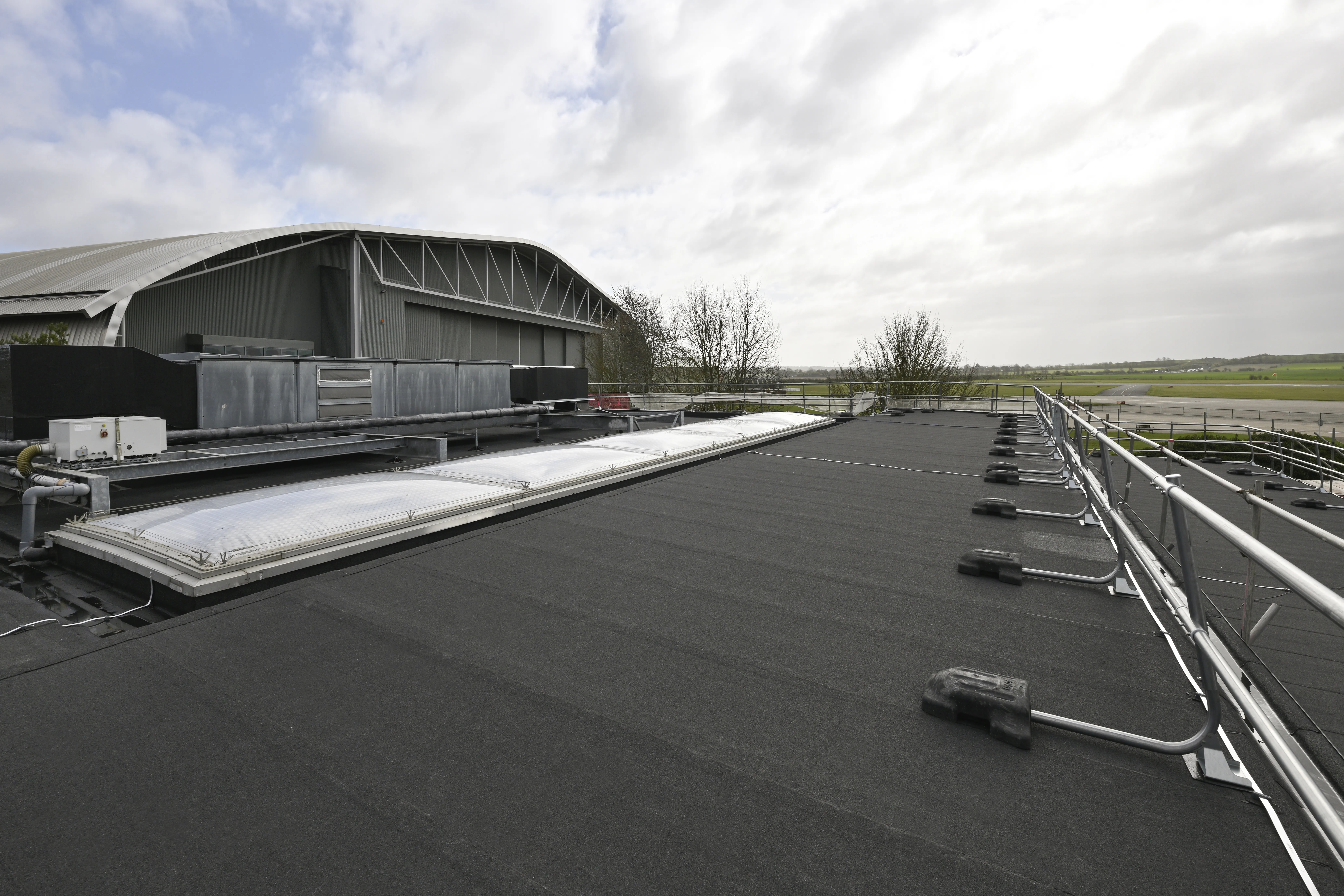 Flat rooftop with solar panels under cloudy sky. Industrial buildings in background.