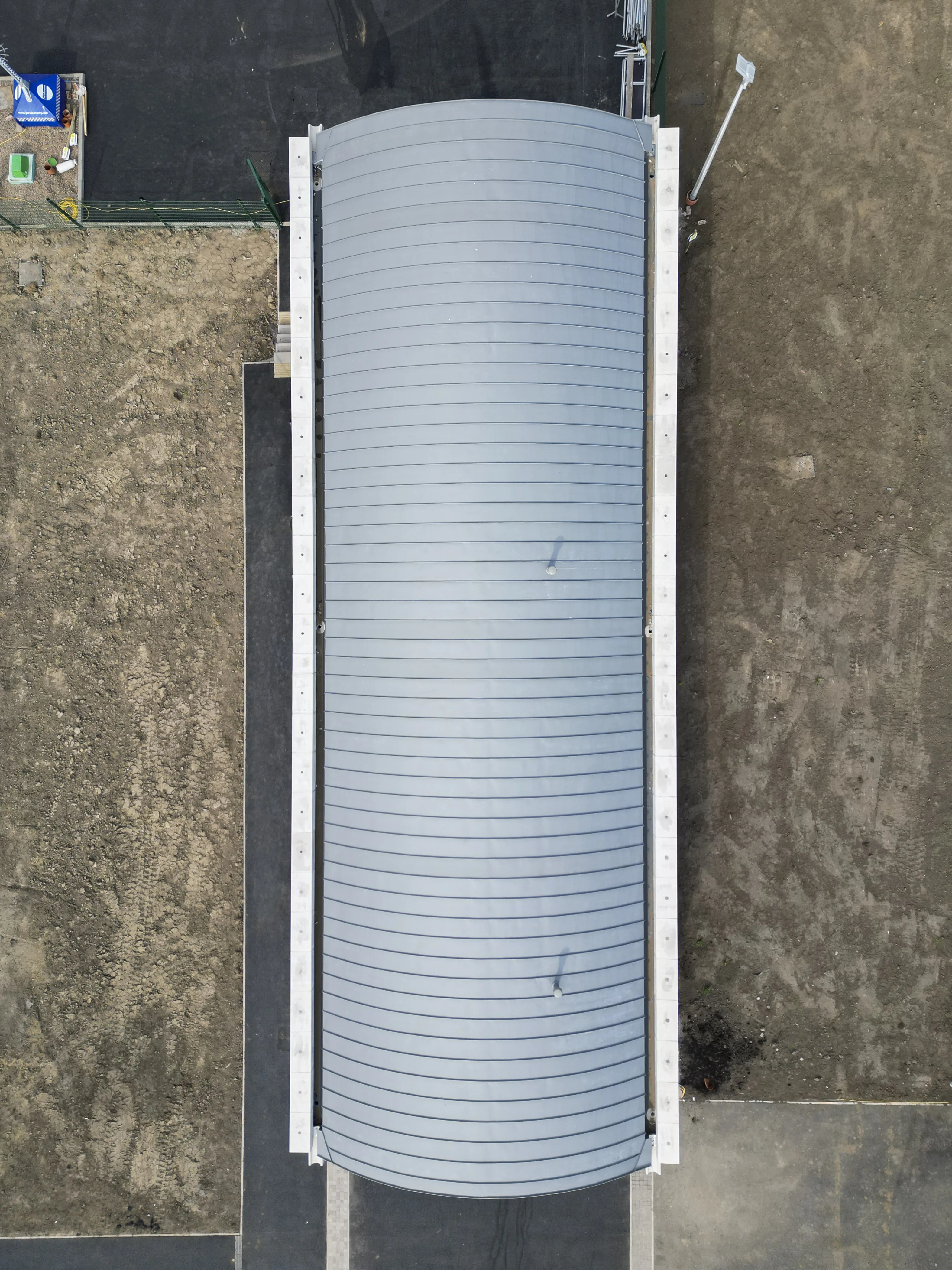 Curved metal structure from above, surrounded by grass and pavement.