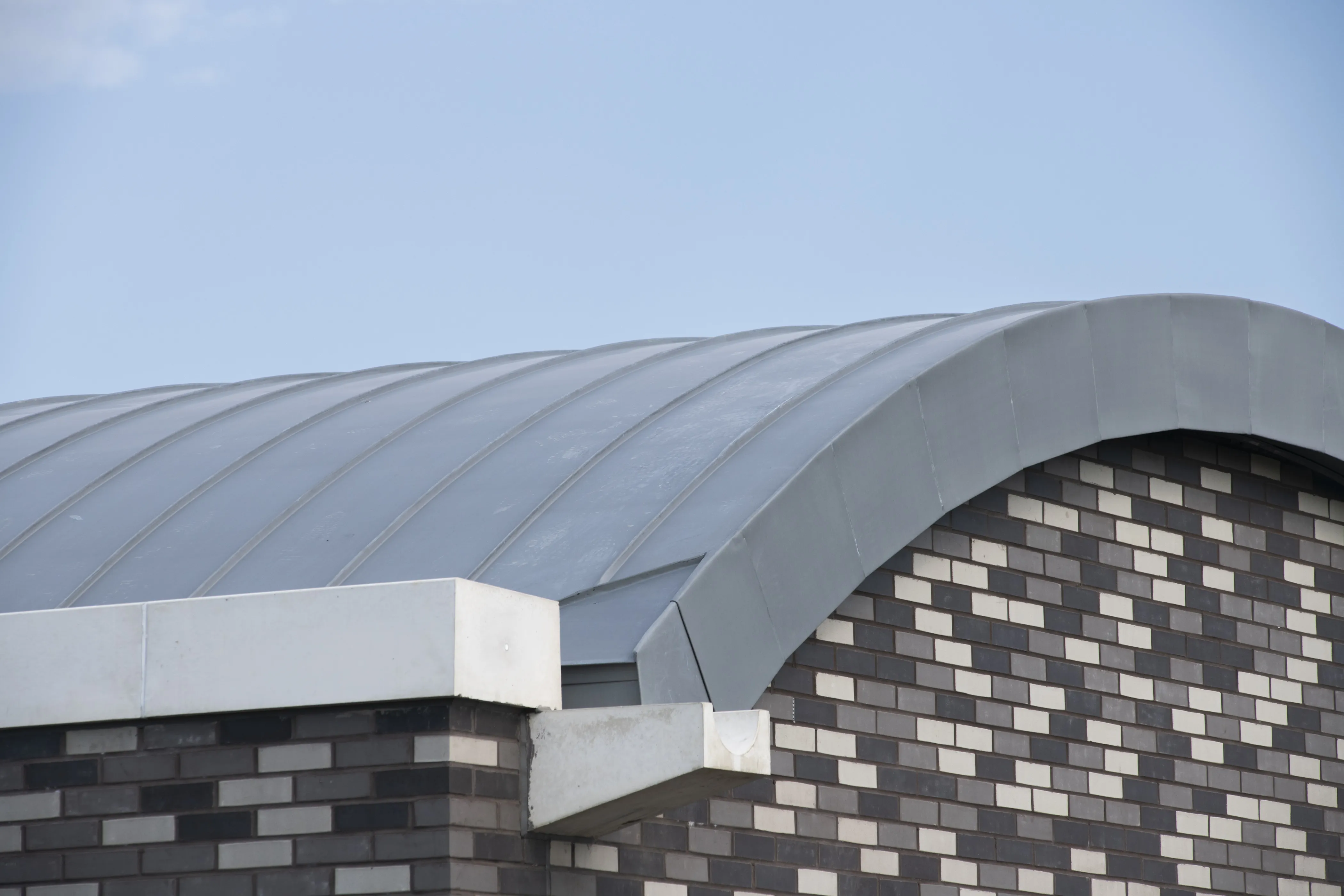 Curved metal roof on a brick building under a clear blue sky.