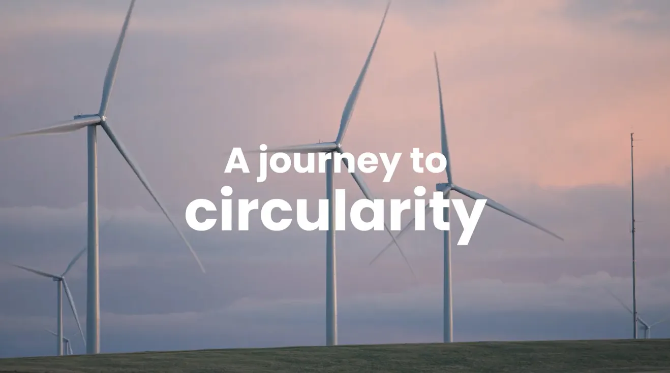 Wind turbines on a hill at sunset, sky pink and cloudy.