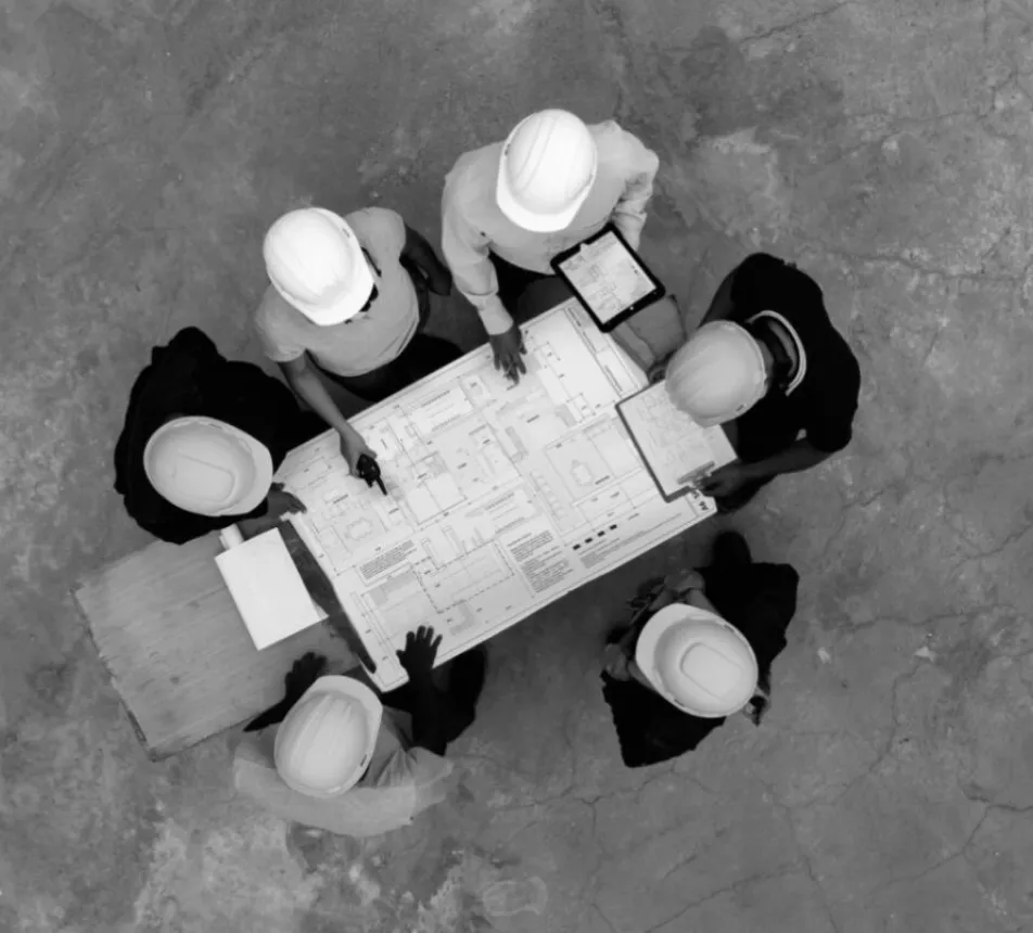 Six people with hard hats reviewing blueprints at a table.