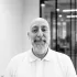 Bald man with a beard, wearing a white polo shirt, in an office setting.